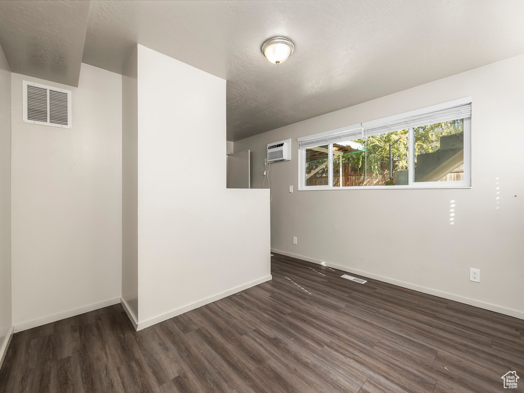 Empty room featuring dark hardwood / wood-style flooring, a textured ceiling, and a wall mounted AC