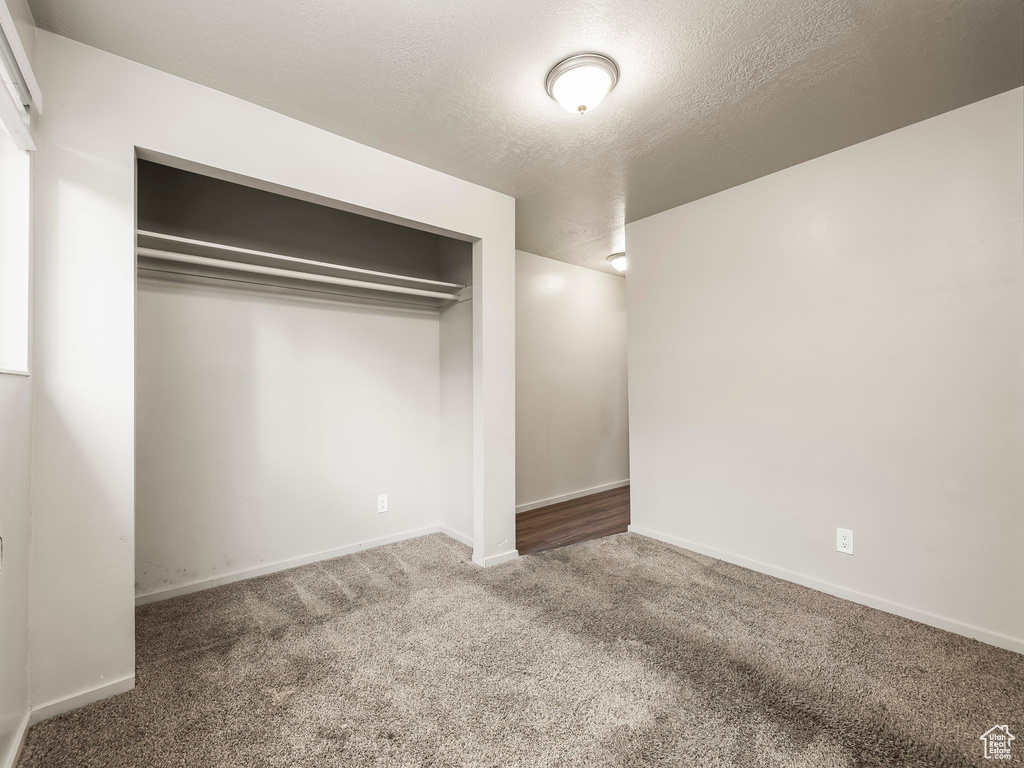 Unfurnished bedroom featuring carpet flooring, a textured ceiling, and a closet