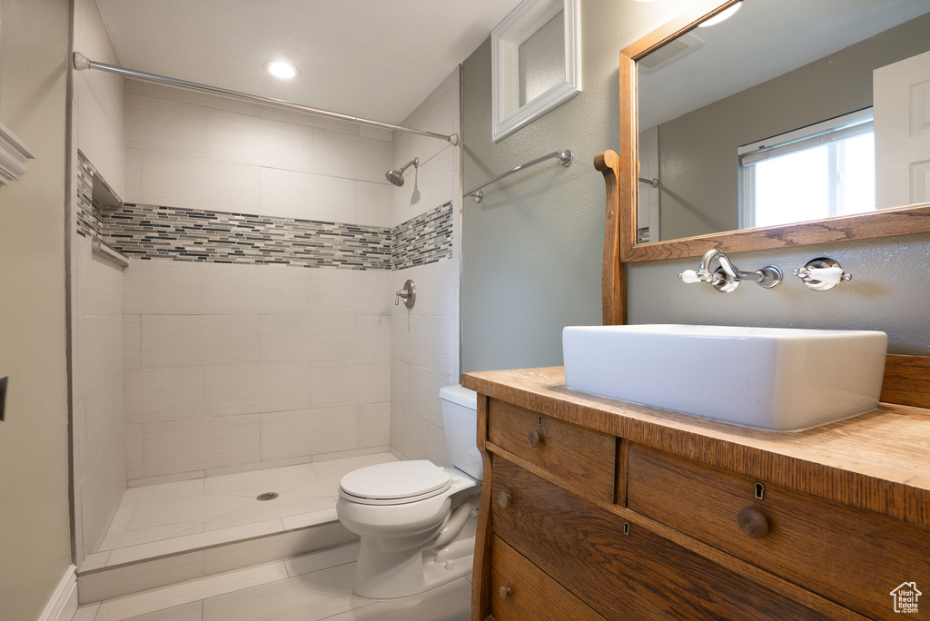 Bathroom featuring a tile shower, tile patterned flooring, vanity, and toilet