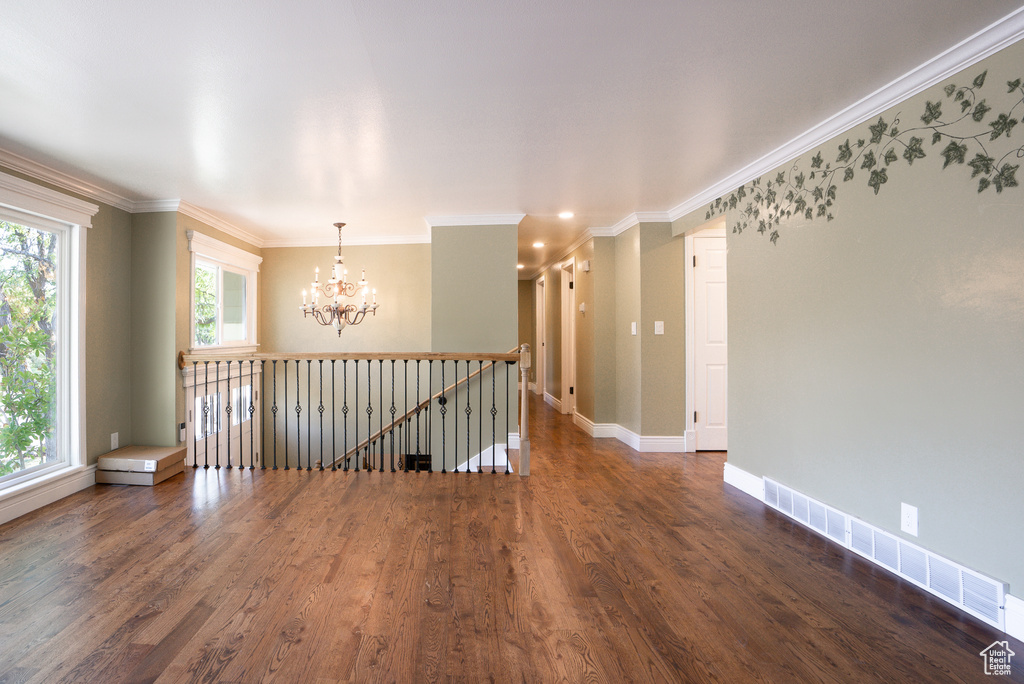 Empty room with ornamental molding, dark wood-type flooring, and a chandelier