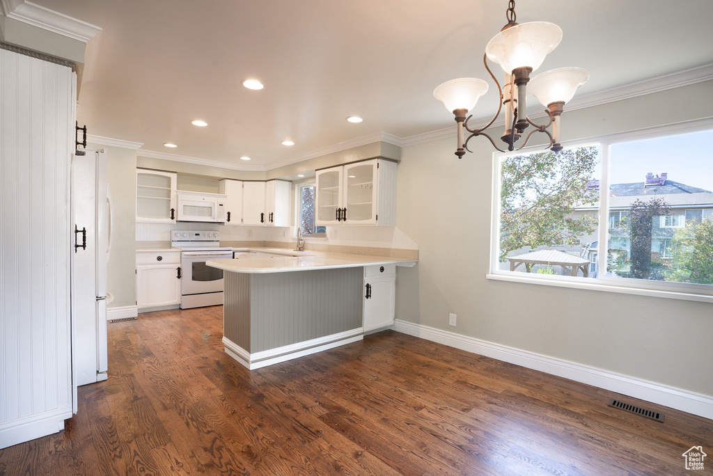 Kitchen featuring white cabinetry, hanging light fixtures, dark hardwood / wood-style floors, kitchen peninsula, and white appliances