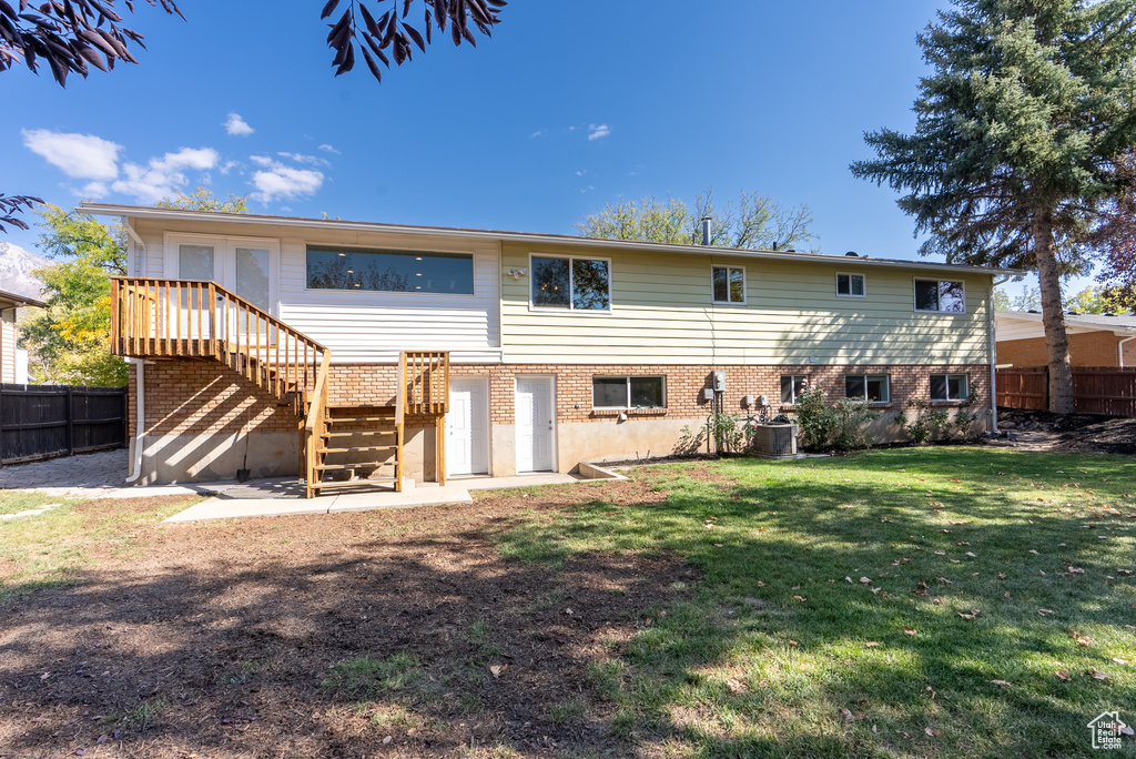 Back of property with central AC, a yard, and a wooden deck