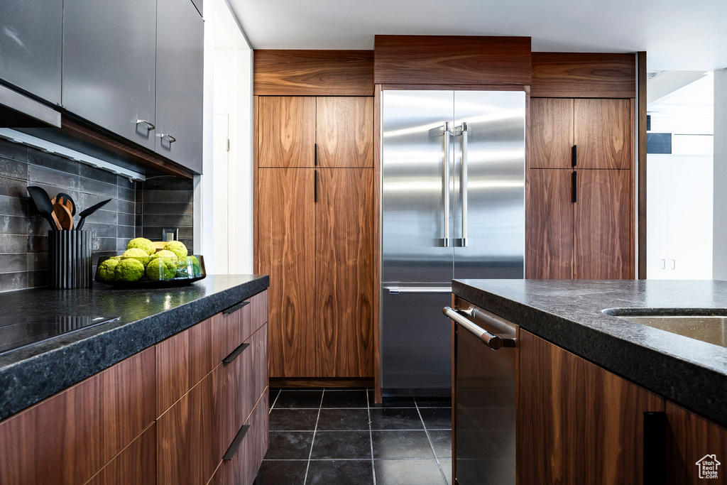 Kitchen featuring stainless steel built in refrigerator, decorative backsplash, and dark tile patterned flooring