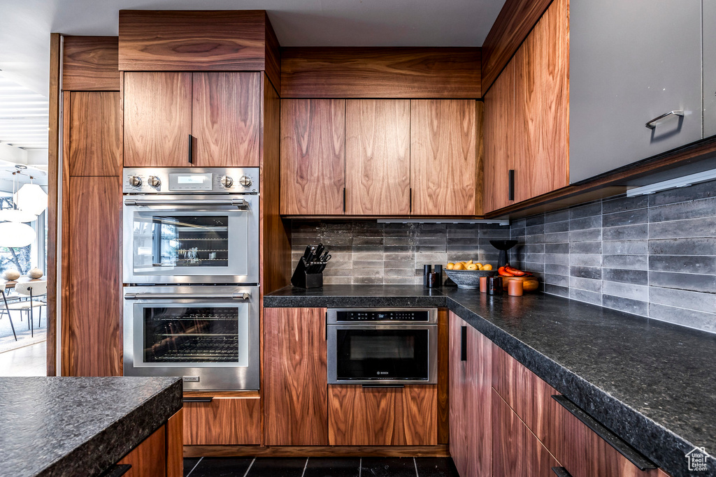 Kitchen featuring dark tile patterned floors, stainless steel double oven, and backsplash