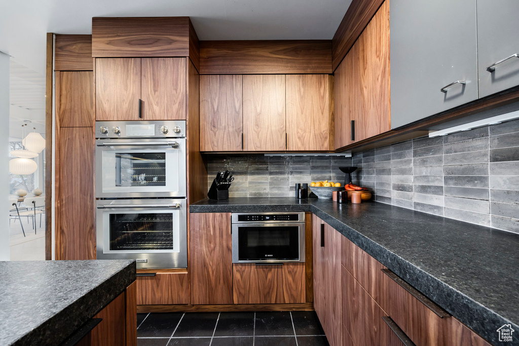 Kitchen with dark tile patterned flooring, stainless steel double oven, and tasteful backsplash