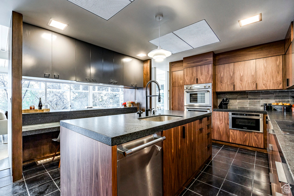 Kitchen featuring pendant lighting, sink, decorative backsplash, an island with sink, and stainless steel appliances