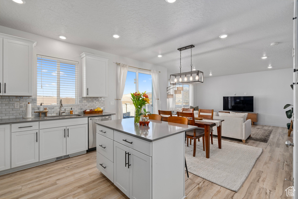 Kitchen with white cabinetry, sink, dishwasher, light hardwood / wood-style flooring, and decorative light fixtures