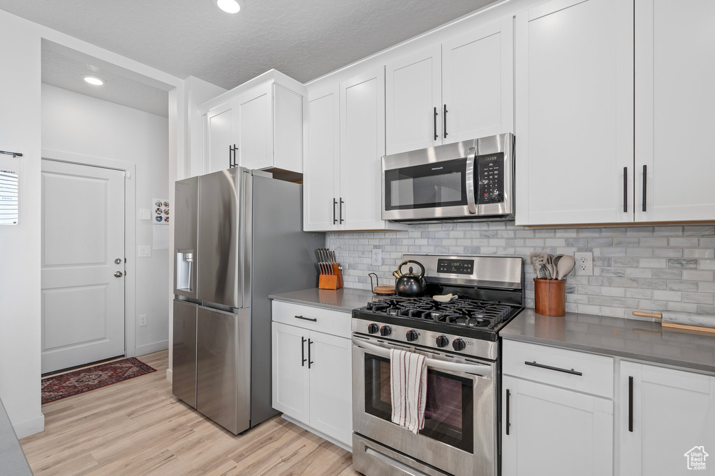 Kitchen featuring tasteful backsplash, appliances with stainless steel finishes, a textured ceiling, white cabinets, and light wood-type flooring