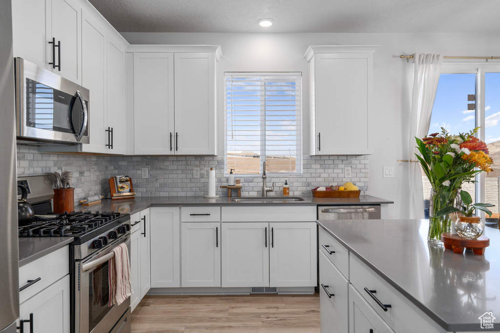 Kitchen featuring white cabinets, sink, light hardwood / wood-style flooring, decorative backsplash, and stainless steel appliances