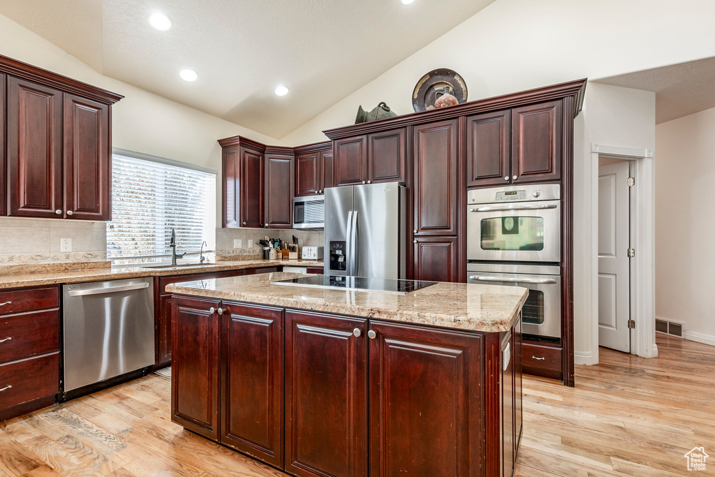 Kitchen with sink, light hardwood / wood-style flooring, vaulted ceiling, a kitchen island, and stainless steel appliances