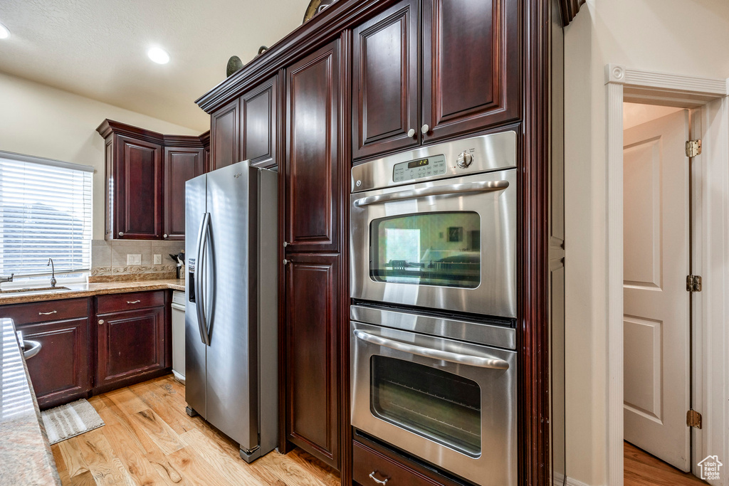 Kitchen with light wood-type flooring, tasteful backsplash, light stone counters, stainless steel appliances, and sink