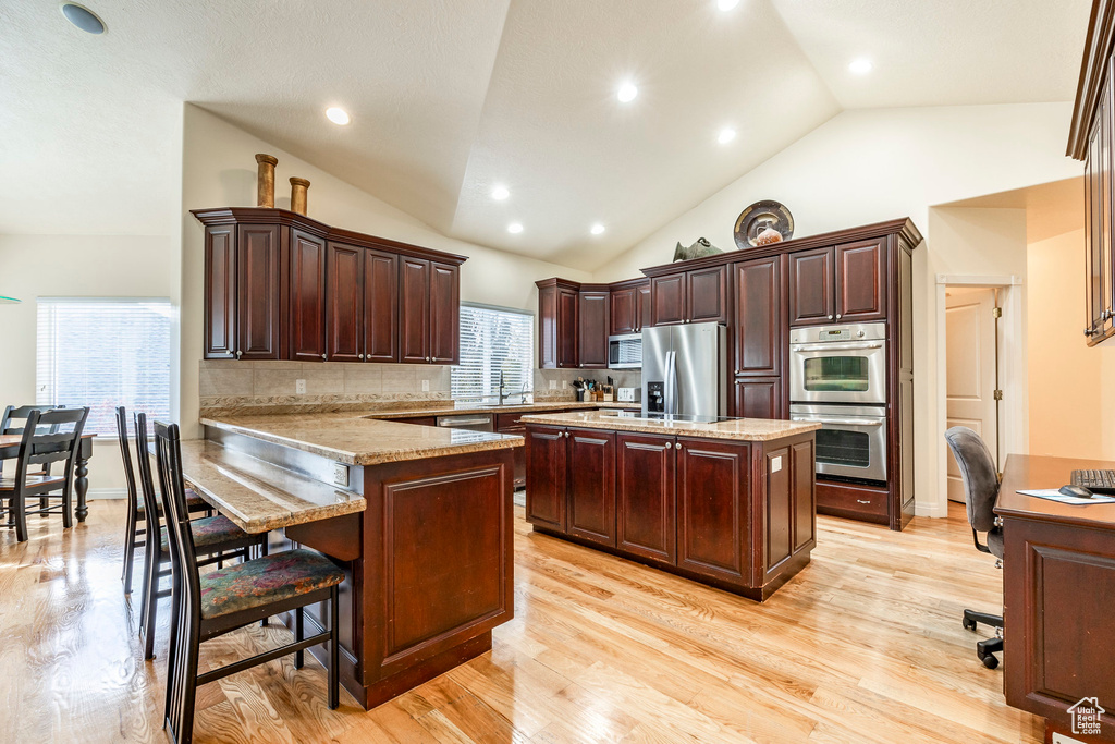 Kitchen featuring backsplash, light wood-type flooring, a kitchen island, kitchen peninsula, and stainless steel appliances