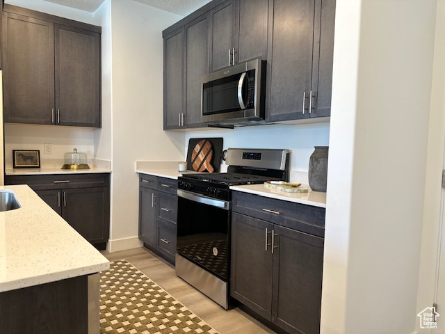 Kitchen with stainless steel appliances, light wood-style flooring, light stone counters, and dark brown cabinetry