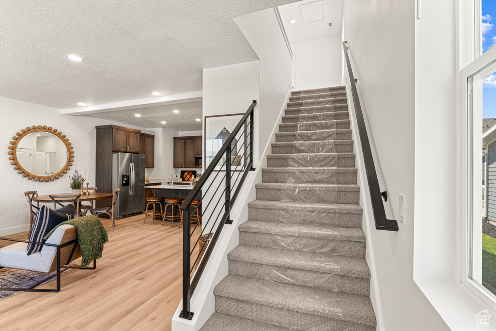 Stairway with wood finished floors, healthy amount of natural light, recessed lighting, and a textured ceiling