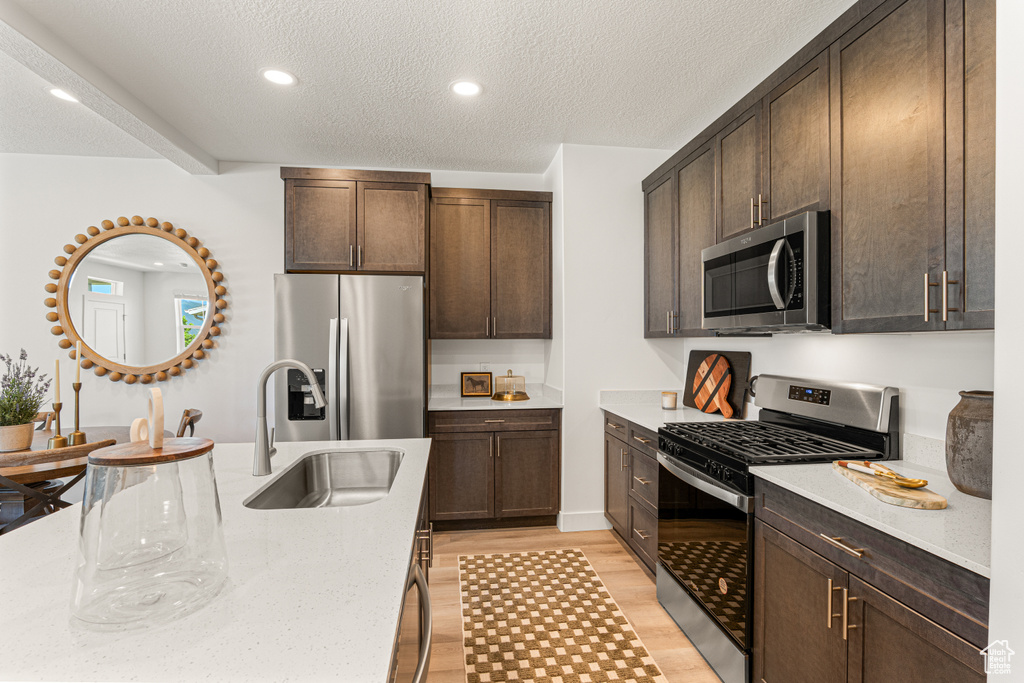 Kitchen with stainless steel appliances, light wood finished floors, dark brown cabinets, a textured ceiling, and recessed lighting