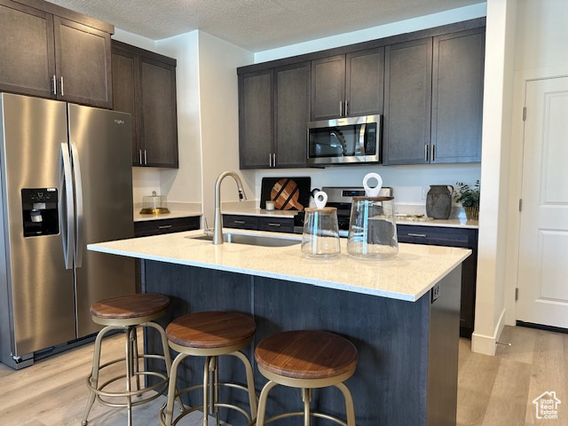 Kitchen with stainless steel appliances, a sink, light wood-type flooring, a breakfast bar area, and a textured ceiling