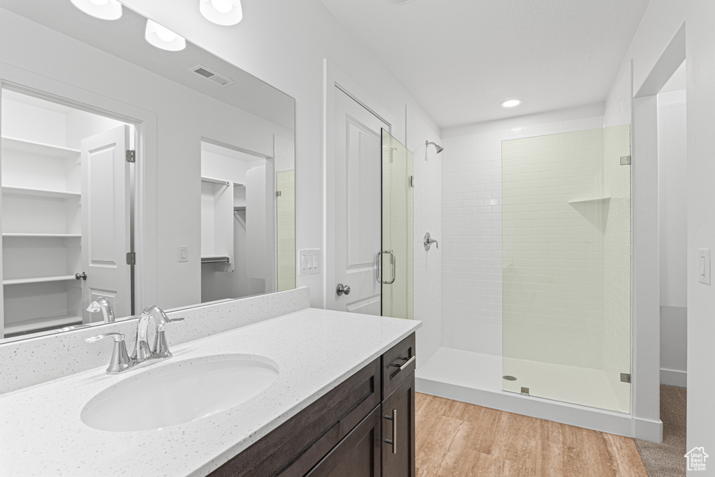 Full bathroom with a stall shower, vanity, a walk in closet, wood finished floors, and recessed lighting