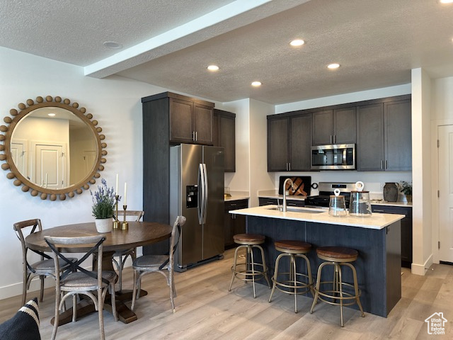 Kitchen with stainless steel appliances, a textured ceiling, light wood-style flooring, a breakfast bar area, and dark brown cabinets
