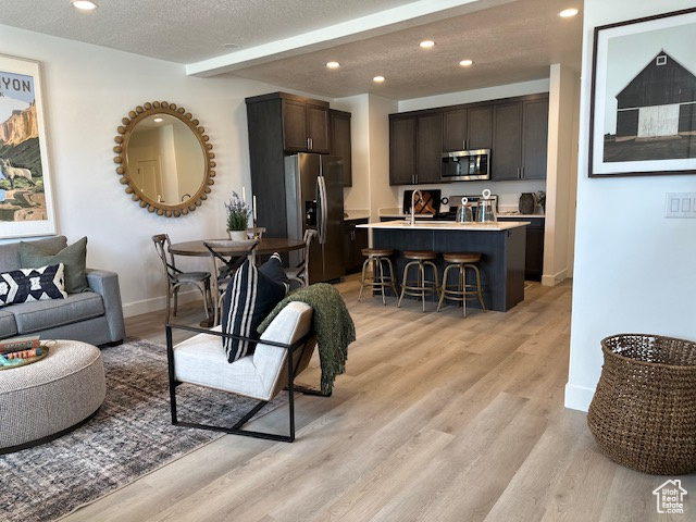 Living area featuring recessed lighting, baseboards, light wood-type flooring, beam ceiling, and a textured ceiling