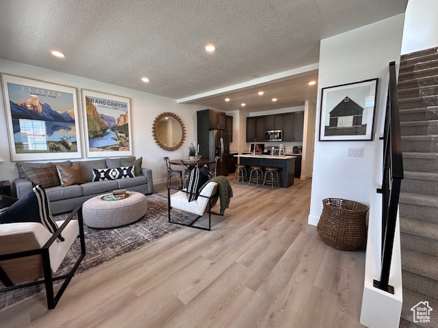 Living room with stairs, light wood-style flooring, a textured ceiling, recessed lighting, and baseboards