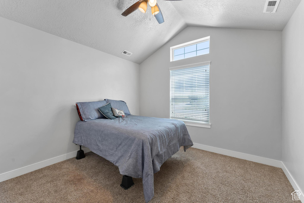 Bedroom featuring a textured ceiling, light colored carpet, ceiling fan, and lofted ceiling