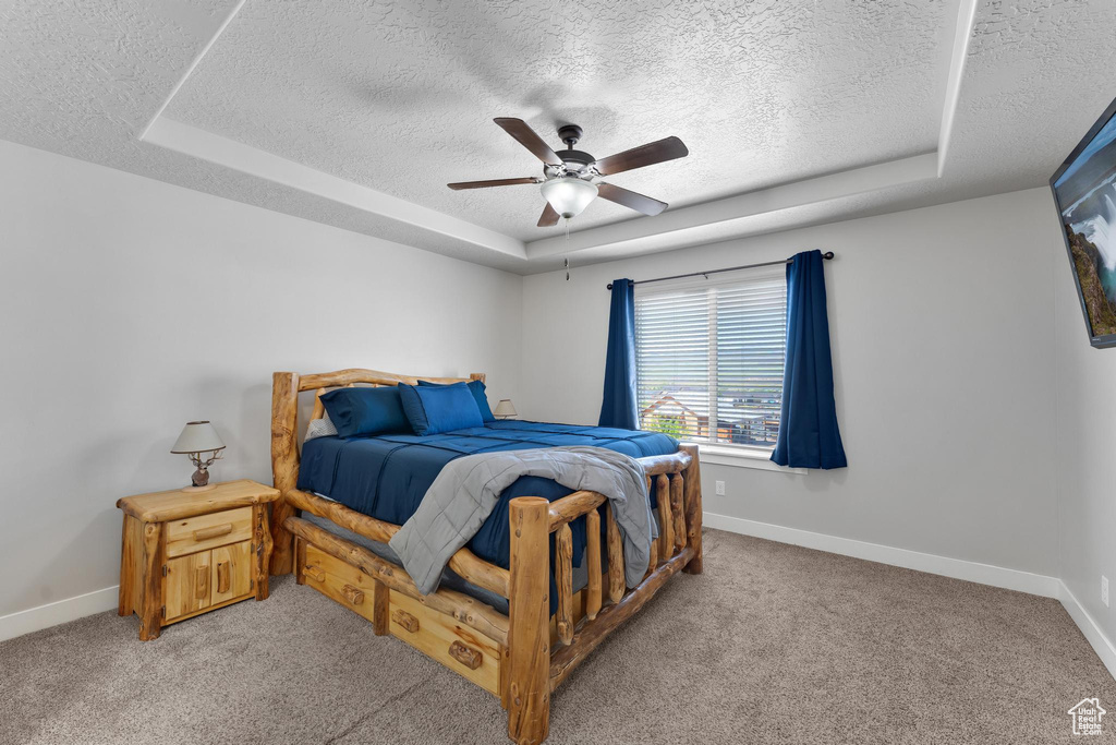 Carpeted bedroom with a textured ceiling, a tray ceiling, and ceiling fan