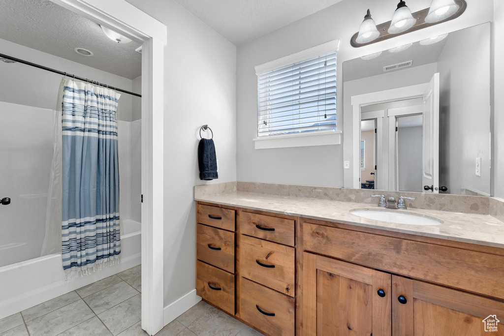 Bathroom with a textured ceiling, tile patterned flooring, vanity, and shower / bath combo