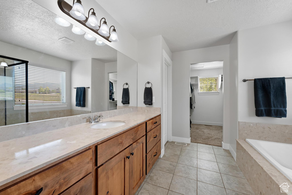 Bathroom featuring tile patterned floors, vanity, a textured ceiling, and tiled bath