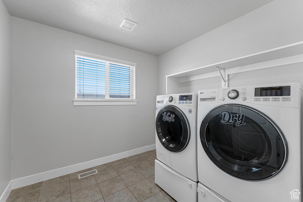 Clothes washing area with washing machine and dryer, light tile patterned flooring, and a textured ceiling