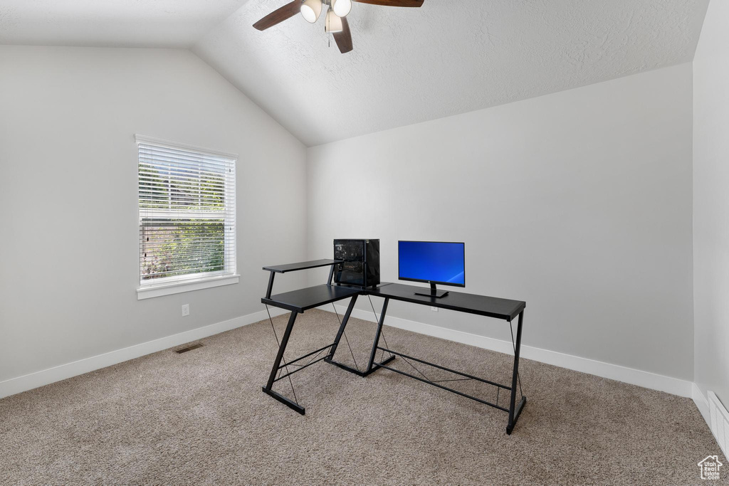 Home office with a textured ceiling, carpet floors, vaulted ceiling, and ceiling fan