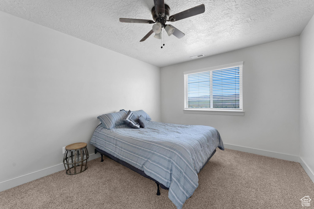 Carpeted bedroom featuring ceiling fan and a textured ceiling