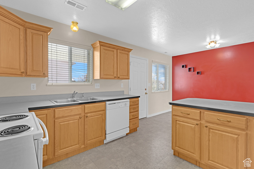 Kitchen with a textured ceiling, white appliances, sink, and light brown cabinetry