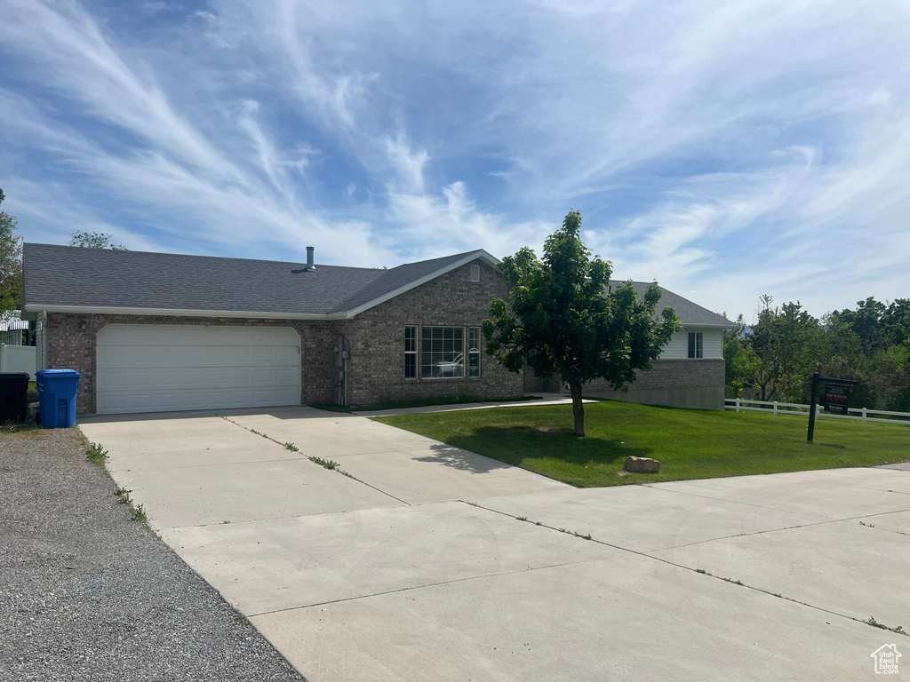 Ranch-style house featuring driveway, an attached garage, a front lawn, brick siding, and roof with shingles