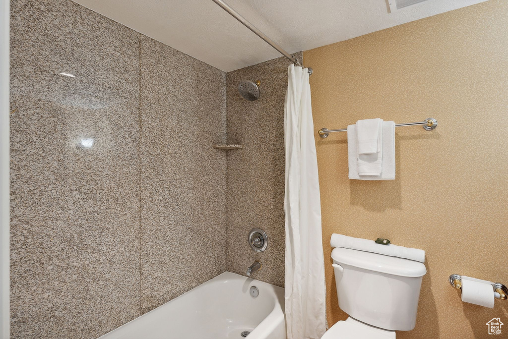 Bathroom featuring shower / bath combination with curtain, toilet, and a textured ceiling