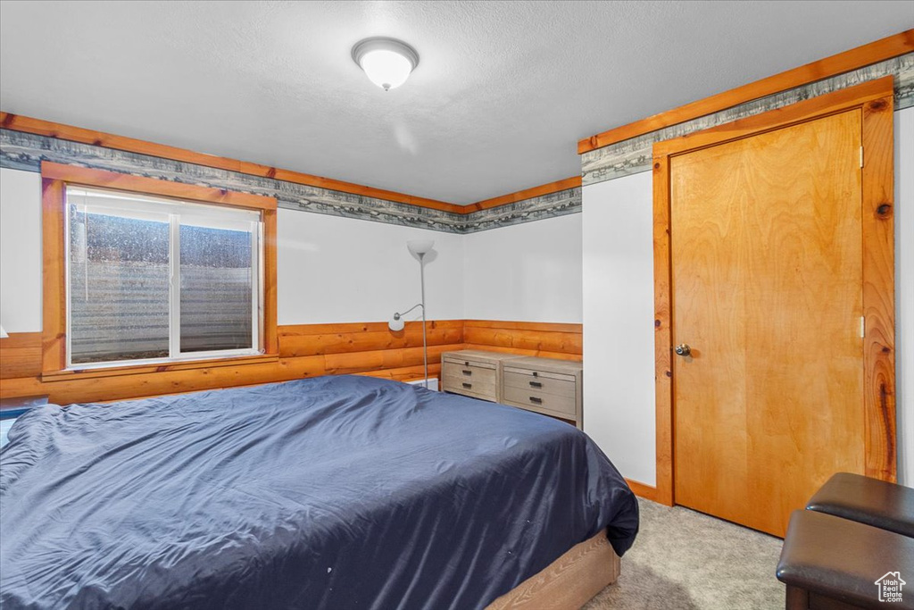 Bedroom featuring wooden walls, light colored carpet, and a textured ceiling