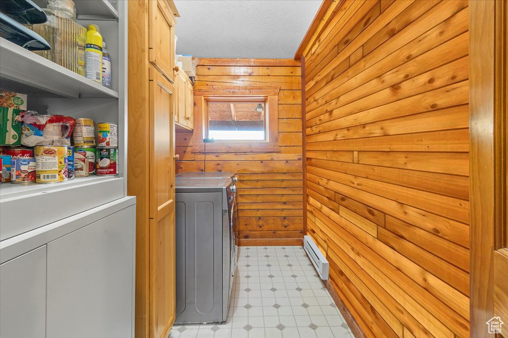 Laundry area with washing machine and clothes dryer, baseboard heating, cabinets, and wood walls