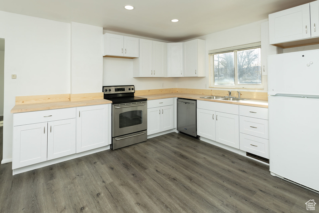 Kitchen featuring dark wood-type flooring, sink, appliances with stainless steel finishes, white cabinetry, and butcher block counters