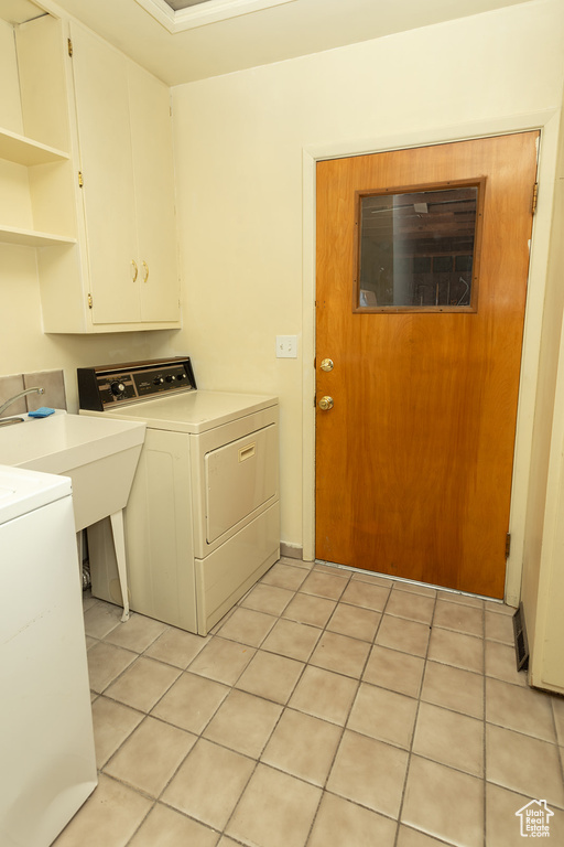 Clothes washing area with washer and clothes dryer, cabinets, light tile patterned floors, and sink
