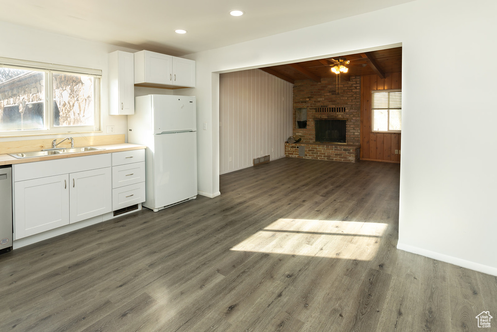 Kitchen featuring dark wood-type flooring, white refrigerator, sink, beamed ceiling, and white cabinetry