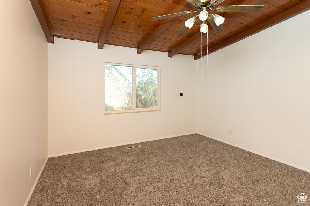 Spare room with ceiling fan, beamed ceiling, wooden ceiling, and dark colored carpet
