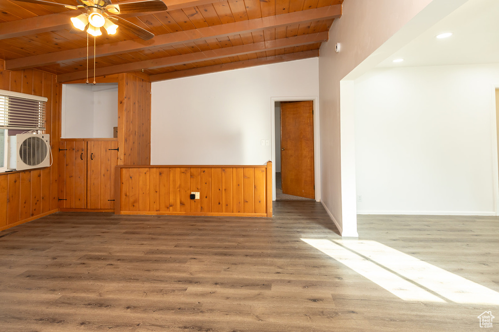 Empty room featuring hardwood / wood-style floors, wood walls, wooden ceiling, lofted ceiling with beams, and ceiling fan