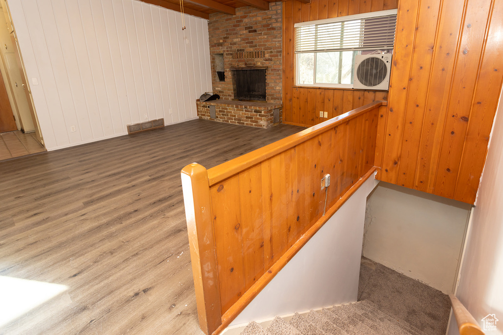 Interior space with hardwood / wood-style floors, ac unit, wooden walls, a brick fireplace, and beamed ceiling