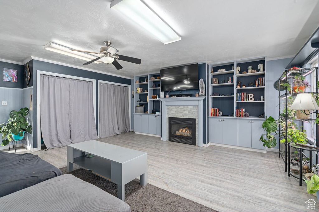 Living room featuring ceiling fan, crown molding, a textured ceiling, a fireplace, and light wood-type flooring