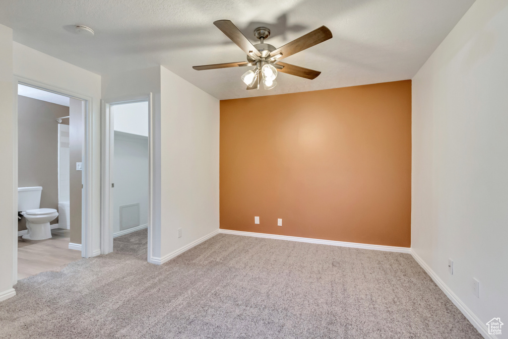 Unfurnished bedroom featuring ensuite bath, ceiling fan, light colored carpet, and a spacious closet