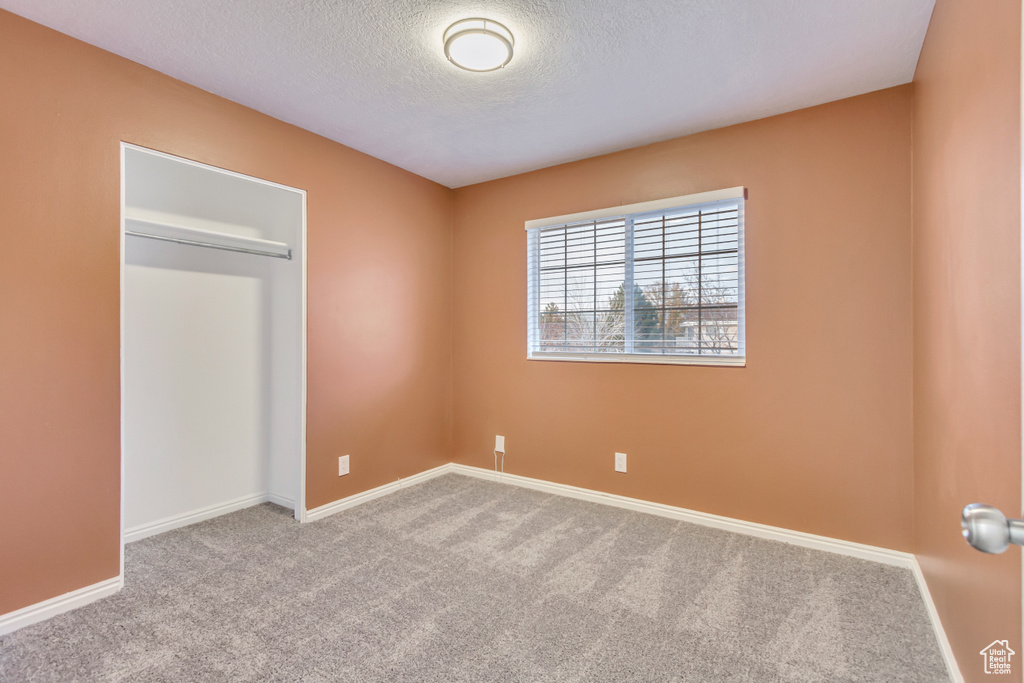 Unfurnished bedroom with light colored carpet, a textured ceiling, and a closet