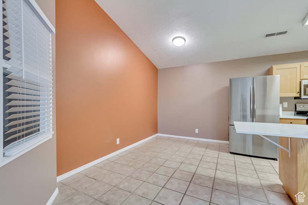 Kitchen with lofted ceiling, light tile patterned floors, a textured ceiling, range, and stainless steel refrigerator
