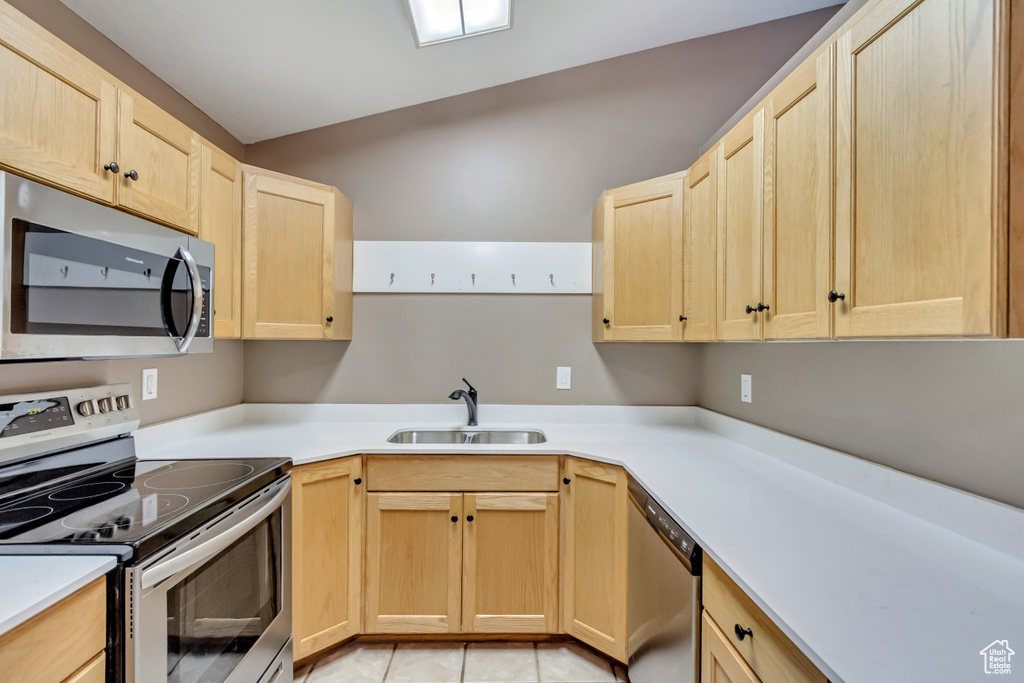 Kitchen featuring light tile patterned floors, lofted ceiling, sink, and appliances with stainless steel finishes
