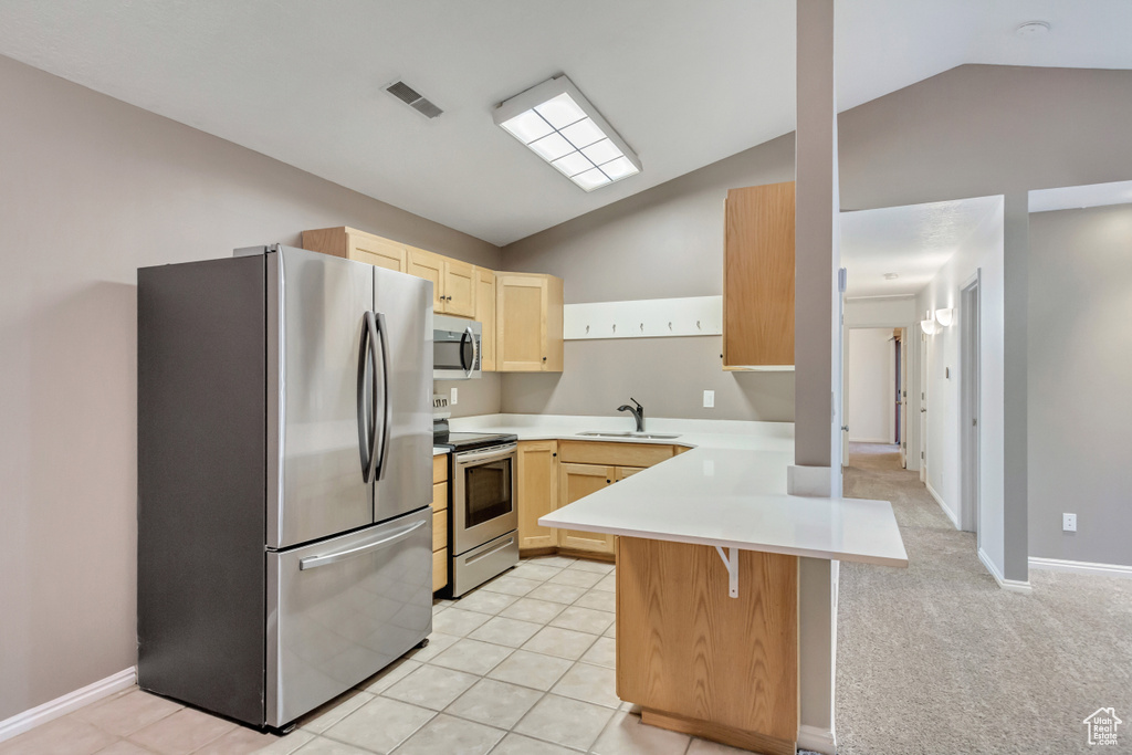 Kitchen featuring kitchen peninsula, a kitchen bar, stainless steel appliances, vaulted ceiling, and light brown cabinets