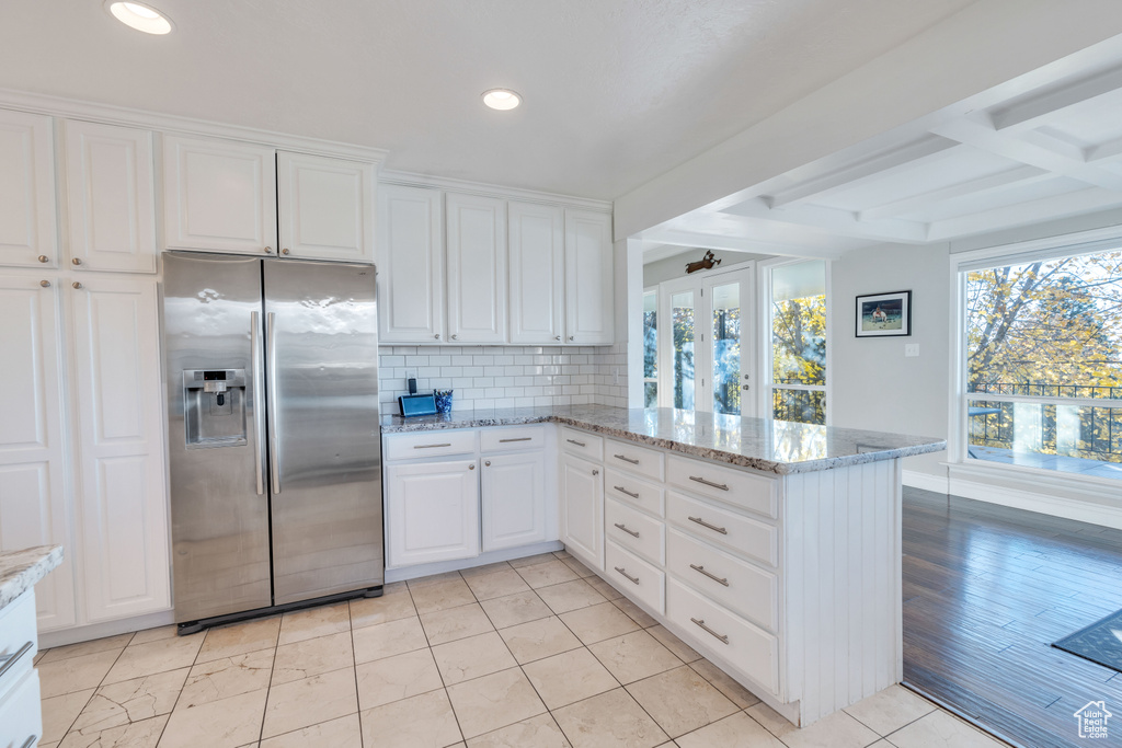 Kitchen with kitchen peninsula, stainless steel fridge with ice dispenser, white cabinets, and light stone countertops