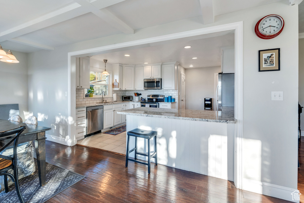 Kitchen with backsplash, light hardwood / wood-style flooring, appliances with stainless steel finishes, beamed ceiling, and white cabinetry